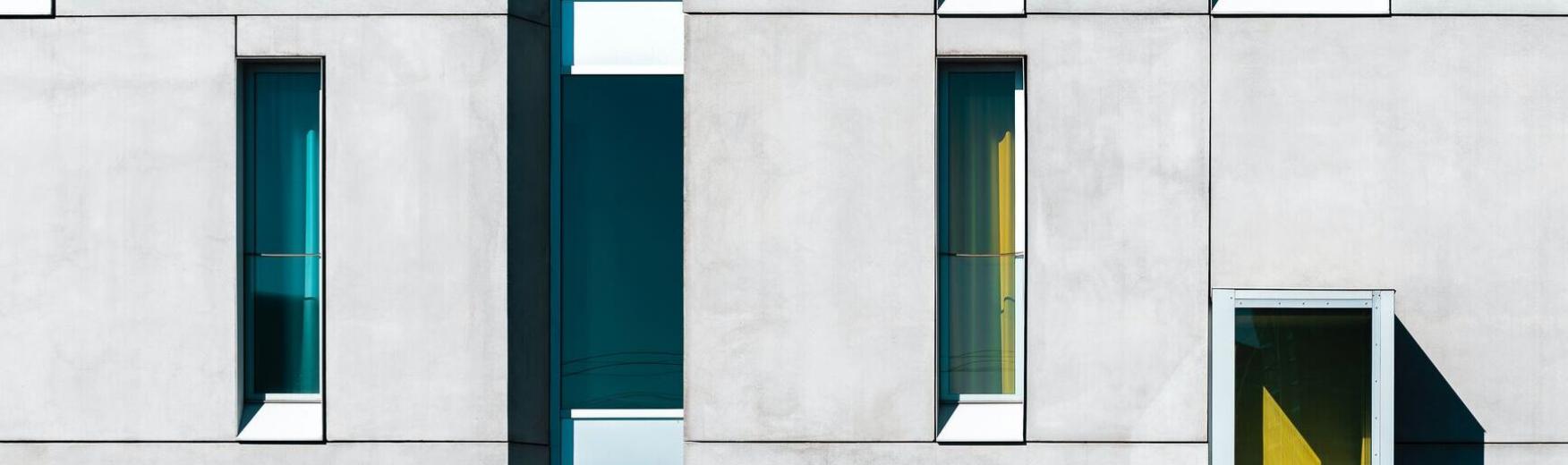 Photo représentant un mur en béton et des fenêtre teintes de différentes couleurs (bleu et jaune)